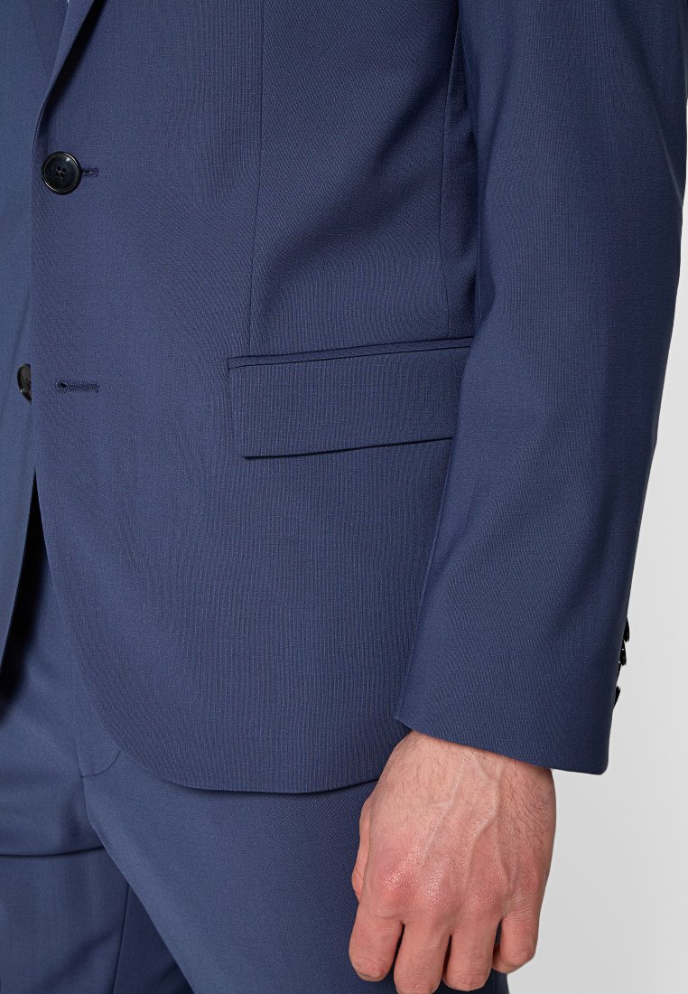 Giacca da abito blu navy realizzata in tessuto strutturato, con un petto singolo, una tasca a soffietto e due bottoni sui polsini per la chiusura.