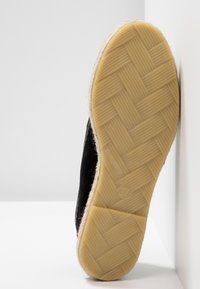 Espadrille noire avec une semelle texturée en caoutchouc présentant un motif tissé. Le bord est enroulé de jute de couleur claire. Taille 37 visible.