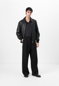 Black leather bomber jacket with ribbed cuffs, paired with a black polo shirt and wide-leg trousers. The outfit features glossy black shoes.
