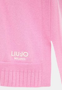 Sezione di maglione rosa lavorato a maglia che mostra l'orlo a coste, la fessura laterale e il ricamo bianco con il logo "LIU JO MILANO".