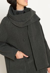 Cappotto grigio scuro con un ampio colletto drappeggiato, due bottoni neri, tasca laterale e texture morbida. Il materiale sembra spesso e caloroso.