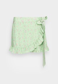 Saia envolvente verde com bainha franzida, apresentando padrões de flores cor-de-rosa. Laços de lado para fechamento e detalhe de textura em camadas.