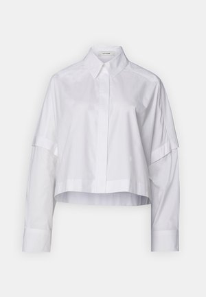 Camisa blanca corta con cuello, de mangas largas y un corte relajado. Está hecha de una tela suave con un diseño limpio y minimalista.