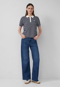 Marineblauwe en witte gestreepte poloshirt met een contrasterende witte kraag, gecombineerd met losse blauwe denim jeans en beige platform schoenen.