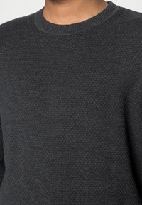 Pull gris foncé en maille avec un motif texturé et un col rond. Le tissu semble doux et légèrement extensible.