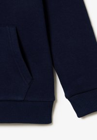 Ύφασμα φούτερ σε ναυτικό μπλε χρώμα με μπροστινή τσέπη και ριμπ μανσέτες. Η υφή φαίνεται λεία και απαλή, με κλασικό, casual σχέδιο.