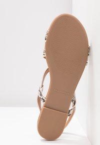 Sandale avec semelle marron clair et semelle en caoutchouc texturée, avec des brides à imprimé serpent beige et noir et le texte "CALL IT SPRING" sur la semelle.
