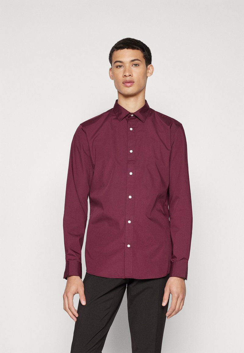 Camisa burdeos de manga larga con diseño de botones en el frente, collar puntiagudo y botones blancos. La tela parece suave con una silueta ajustada.