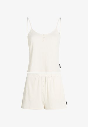 Completo loungewear bianco a costine composto da una maglietta senza maniche con bottoni e pantaloni corti abbinati con vita elasticizzata. Morbido al tatto e vestibilità comoda.