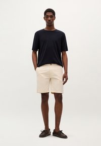 Tricou navy cu guler rotund, asortat cu pantaloni scurți bej deschis, confecționați din bumbac, având închidere cu nasturi și buzunare laterale, purtat cu pantofi închiși la culoare.