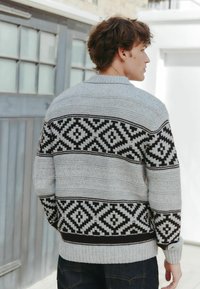 Grå og sort mønstret sweater med et geometrisk design, ribbede manchetter og kant, samt en lige silhuet. Strikket struktur.