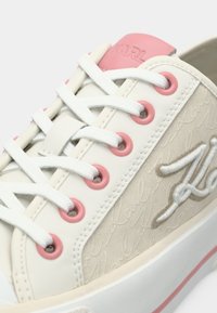 Λευκό αθλητικό παπούτσι με ροζ οπές και λεπτομέρειες, με υφή στην πλευρά που φέρει λογότυπο και σύστημα κορδονιών, κατασκευασμένο από συνθετικά υλικά.