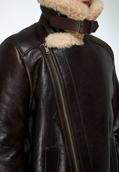 Veste en cuir marron avec col en peau lainée, dotée d'une fermeture éclair diagonale et de poches latérales, mettant en valeur une texture lisse et un design ajusté.