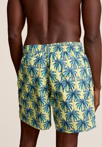 Zwemshorts met een gele achtergrond, voorzien van een palmbomenpatroon in blauw en groen, elastische tailleband en zijzakken.