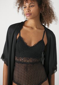 Zwart kanten bodysuit met bloemenprint, doorzichtige mesh delen en verstelbare bandjes, gecombineerd met een zwart satijnen kimono met kantranden.