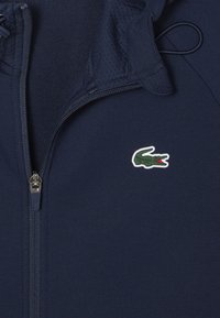 Navy blue zip-up jacket with hood, featuring a small green crocodile logo on the left chest.