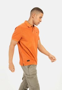 Oranje polo shirt met een klassieke kraag en twee knopen, korte mouwen, zijsplitsen, gecombineerd met lichte kaki cargobroek.