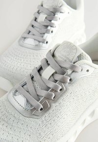 Baskets de sport gris clair avec une tige en tricot texturé, des œillets métalliques et des lacets plats. Dotées d'un collier rembourré et d'un logo sur la languette.