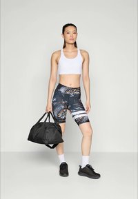 Čierna športová taška, biely športový top, vzorované šortky v odtieňoch modrej, oranžovej a černej. Model má na sebe čierne tenisky a biele ponožky.