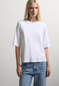 T-shirt bianco in cotone a maniche corte con scollatura a girocollo e vestibilità rilassata, indossato con un paio di jeans in denim azzurri a vita alta.