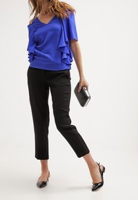 Blå off-shoulder topp med volangdetaljer, i kombination med svarta slim-fit byxor och svarta ballerinas. Accessoarerna inkluderar en silverfärgad kuvertväska.