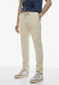 Krémové bavlněné kalhoty s pružným pasem, se bočními kapsami. Doplňují je šedé a bílé tenisky s jemnými akcenty.