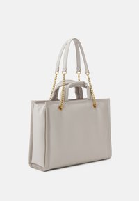 Sac à main en toile gris clair avec une texture lisse, deux poignées supérieures et des accents en chaîne dorée. Forme rectangulaire avec des côtés structurés.