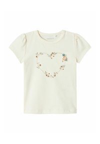 Kortærmet, cremefarvet bomulds t-shirt med et hjerteformet blomsterbroderi design og en lille stofrose accent på venstre side.