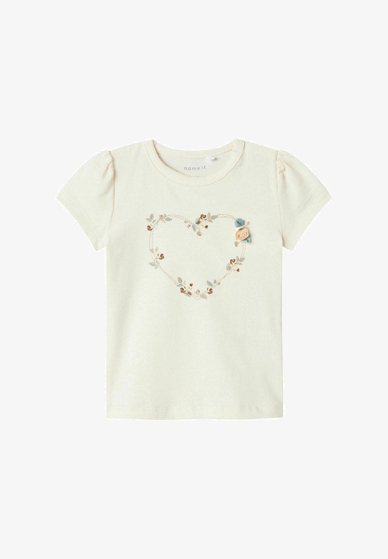 Kortærmet, cremefarvet bomulds t-shirt med et hjerteformet blomsterbroderi design og en lille stofrose accent på venstre side.