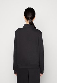 Svart sweatshirt med hög krage, långa ärmar och ribbade mudd. Slät textur och avslappnad passform, sedd från baksidan.