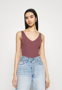 Geribbelde, v-hals body in gedempt mauve, gecombineerd met lichtblauwe high-waisted denim jeans. Soepele textuur, minimalistisch ontwerp.