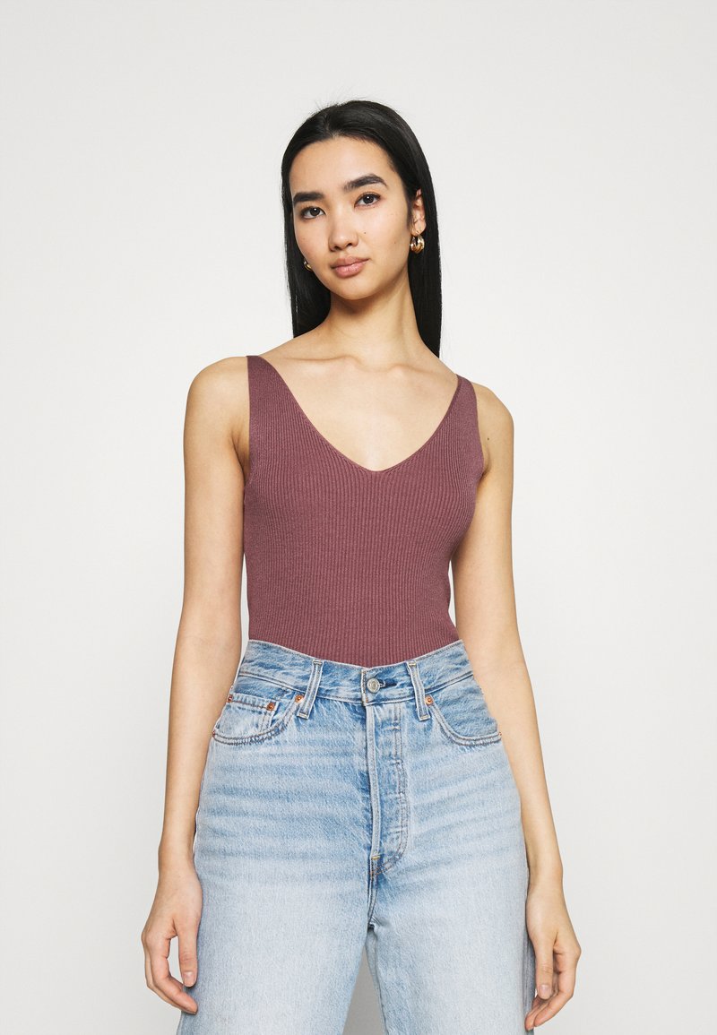 Prążkowany bodysuit w kształcie v-neck w stonowanym mauve, w połączeniu z jasnoniebieskimi jeansami z wysokim stanem. Gładka tekstura, minimalistyczny design.