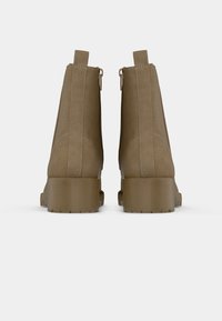 Paire de bottines en daim marron à talons blocs, visibles de dos sur un fond blanc uni.