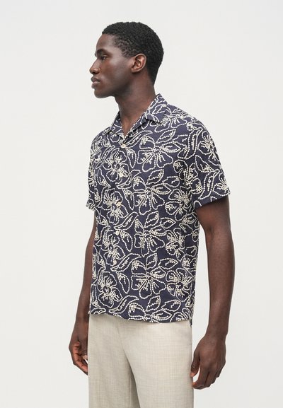 Košeľa s krátkym rukávom v námorníckej modrej farbe s krémovými kvetinovými vzormi. Dizajn s golierom a gombíkmi, má voľný strih a ľahký materiál.