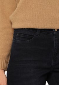 Ciemnoniebieskie dżinsy o subtelnej fakturze, dopasowany krój i klasyczny styl pięciu kieszeni. W zestawie z jasnobrązowym swetrem z dzianiny.
