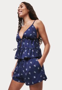 Navy bloemen twee-delig set met een top met ruches aan de onderkant en bijpassende shorts. Kenmerken zijn spaghettibandjes, lichtgewicht stof en zijzakken.