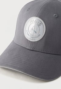 Γκρι υφασμάτινο καπέλο με στρογγυλεμένη κορυφή και κυρτό γείσο. Διαθέτει κυκλικό έμβλημα με τις λέξεις "ΠΑΡΙΣΙ" και "ΣΕΝ-ΖΕΡΜΕΝ" κεντημένες με ασημί κλωστή.