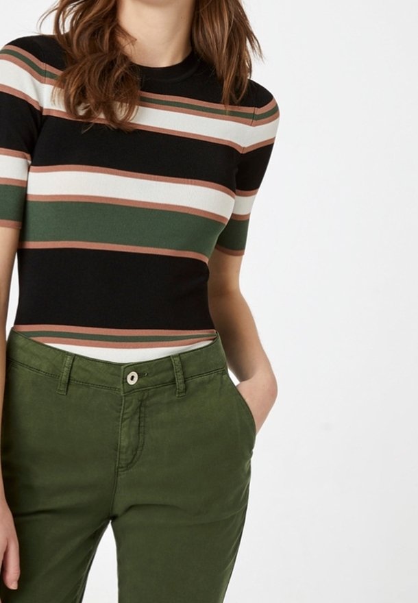 Musta ja raidallinen lyhythihainen paita, jossa on vihreitä, valkoisia ja ruosteisia kuvioita, yhdistettynä oliivinvihreisiin housuihin, joissa on etutasku ja napitus.