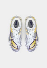 Pár basketbalových bot Puma ve vícebarevném provedení, bílé barvy s žlutými, fialovými a šedými akcenty a bílými tkaničkami, na bílém pozadí.