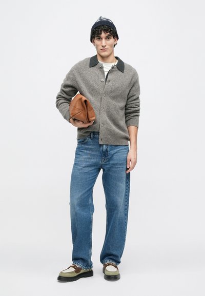 Szürke kötött kardigán fekete gallérral, kék farmernadrág és barna táska. A hétköznapi lábbeli zöld, barna és krémszínű részletekkel rendelkezik.