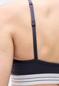 Πλάγια όψη ατόμου που φοράει μαύρο και άσπρο αθλητικό σουτιέν με ρυθμιζόμενους μαύρους ιμάντες, εμφανίζοντας μέρος της άνω πλάτης και του ώμου του.