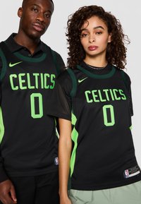 Sorte basketball-drakter med "CELTICS" i lys grønn, med mesh-struktur og grønne detaljer. Nike-merket synlig på skuldrene.