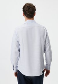 Lange mouwen, lichtblauw shirt met een gestructureerd patroon; heeft een achterste yoke en knopenmanchetten. Zoom is aan de zijkanten gebogen.