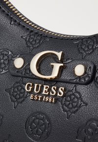 Geantă de mână din piele texturată neagră, cu accesorii din metal auriu, modele florale embosate și un logo 'G' proeminent, precum și numele brandului.