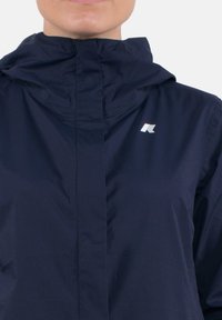 Giacca leggera navy con colletto alto, zip frontale e un piccolo logo bianco sul lato sinistro. Tessuto liscio, materiale resistente all'acqua.
