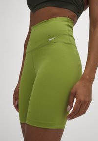 Pantalones cortos verdes con una cinturilla alta, hechos de tela elástica. Presentan un logo blanco en el frente y una textura suave y elegante.