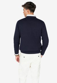 Pullover navy, con polsini e orlo a costine, in tessuto misto cotone. Indossato con pantaloni cargo crema, che mostrano un colore uniforme e un design sportivo.