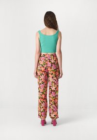 Crop top u tirkiznoj boji, široke hlače s cvjetnim uzorkom u ružičastoj i narančastoj boji te ružičaste sandale na blok petu. Kosa je valovita; model okrenut prema drugoj strani.