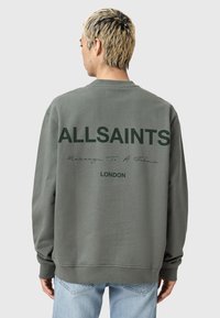 Grå sweatshirt med långa ärmar och rund halsringning. Har stora svarta bokstäver: "ALLSAINTS," "Message To A Future" och "LONDON" på baksidan.