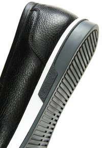 Baskets en cuir noir avec une surface texturée, une forme arrondie, une semelle intermédiaire blanche et une semelle extérieure en caoutchouc gris présentant des rainures horizontales.